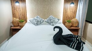 Ein ordentlich bezogenes Bett mit zwei Kissen, einem schwarzen Handtuch in Form eines Schwans und zwei Korbwannen mit Pflanzen auf jeder Seite.