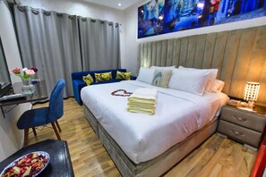 Una camera d'albergo con un letto, una scrivania, una sedia, un comodino e un quadro appeso al muro.