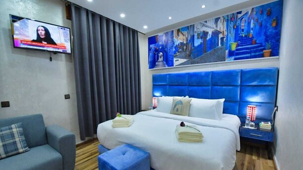 A hotel room with a large bed, a television on the wall, and a blue-themed mural. - Hotel Dar Annasr (Chefchaouen)