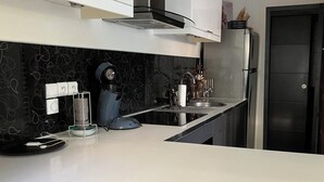 Ett modernt kök med en svart marmorvägg bakom arbetsbänken, rostfria vitvaror och en vit bänkskiva.