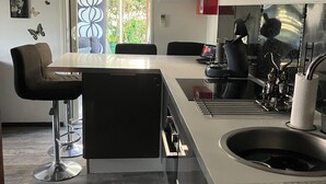 Ett modernt kök med en central köksö, barstolar, en diskho och en spis.