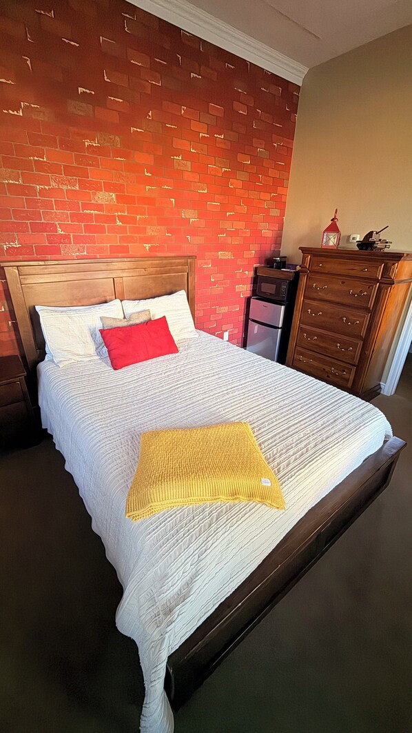 Un lit avec une couette blanche, un oreiller rouge et un plaid jaune.