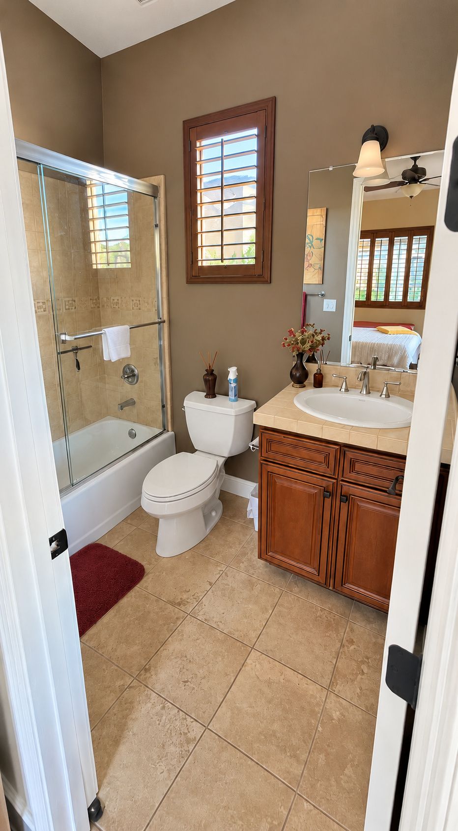 A bathroom with a glass shower enclosure, a toilet, a sink with a vanity, and a window with blinds.