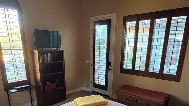 Une chambre avec un grand lit, un ventilateur de plafond, un téléviseur posé sur un meuble, une bibliothèque et une porte avec une fenêtre.