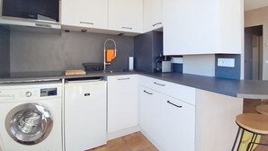 A compact kitchen with white cabinets, a built-in washing machine, a coffee machine, and a small bar area. - Breathtaking panoramic sea view - Exceptional 2P at Le Grand Duc (Mandelieu-la-Napoule)