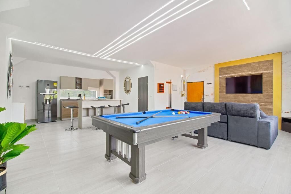 A modern living room with a pool table, a grey sofa, and a TV mounted on a wooden wall.
