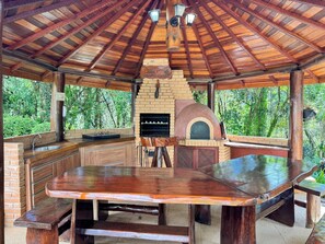 Eine Außenküche mit Backofen aus Ziegelsteinen, Holztischen und einer rustikalen Holzbalkendecke.