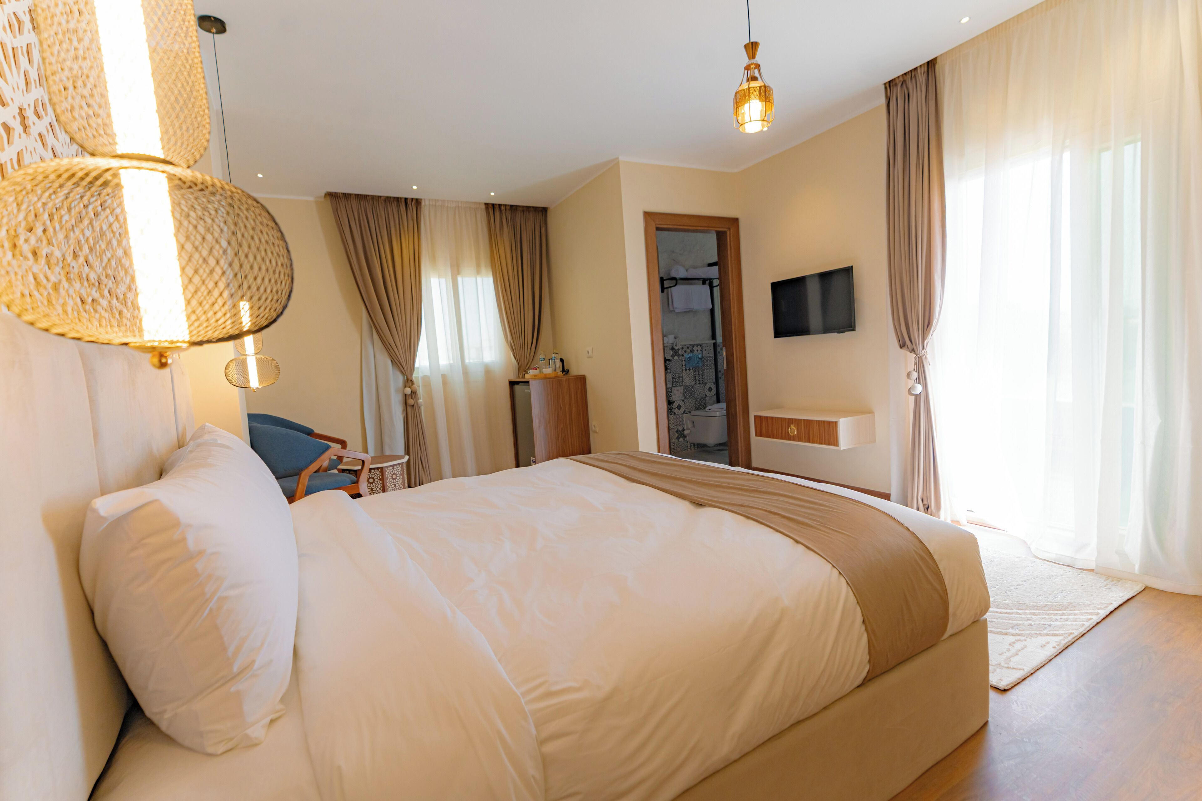 A hotel room with a large bed, a desk, a chair, a TV, and a bathroom visible through an open door.
