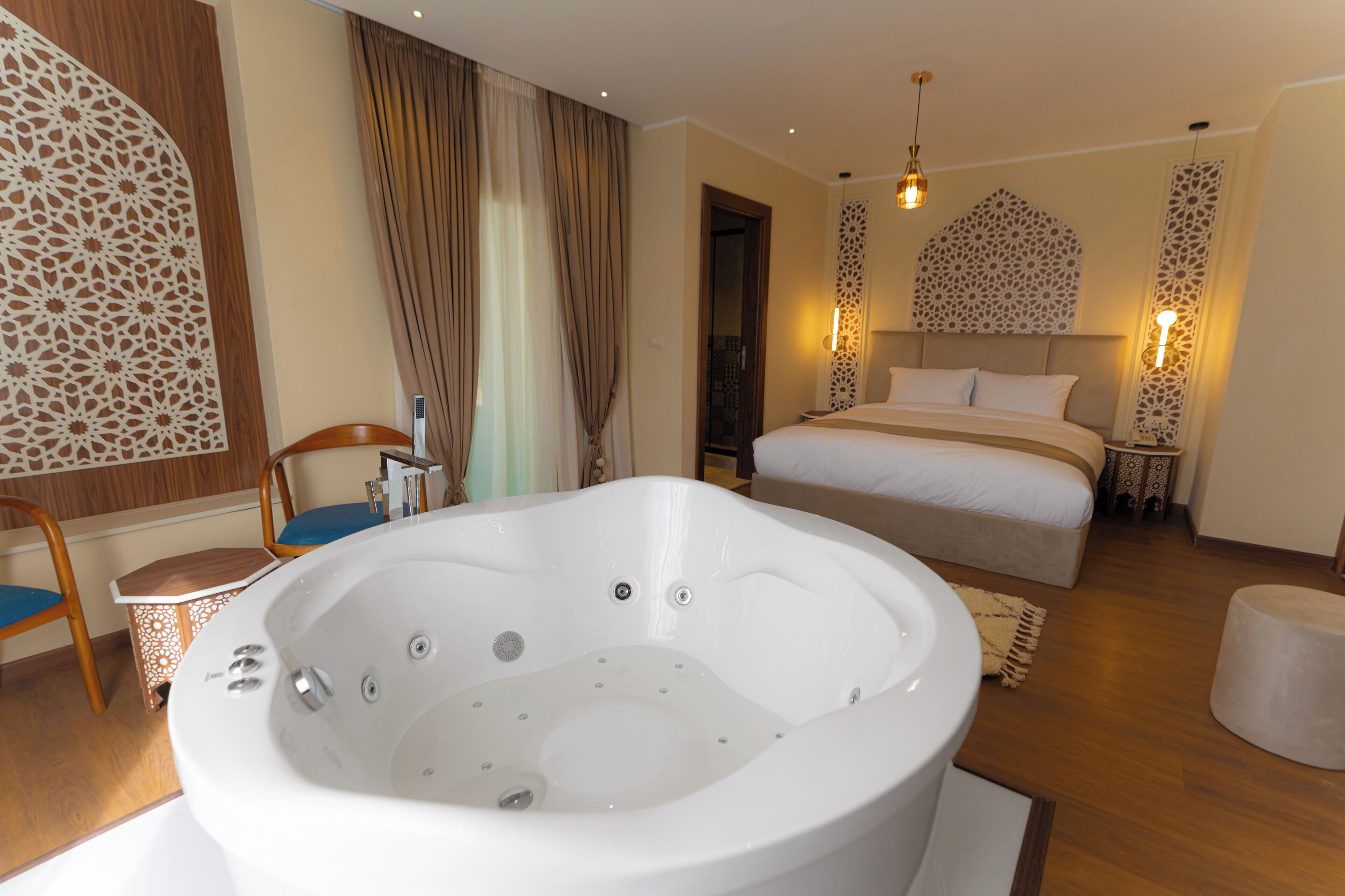 Ein modernes Hotelzimmer mit einer großen Badewanne, einem Bett mit weißen Leinen und dekorativen Wandpaneelen.