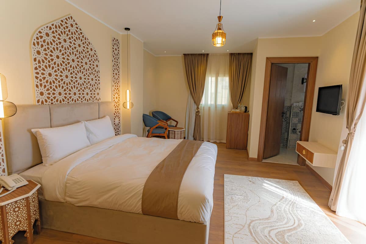 A hotel room with a large bed, a desk with a telephone, a chair, a TV, and a decorative wall panel.