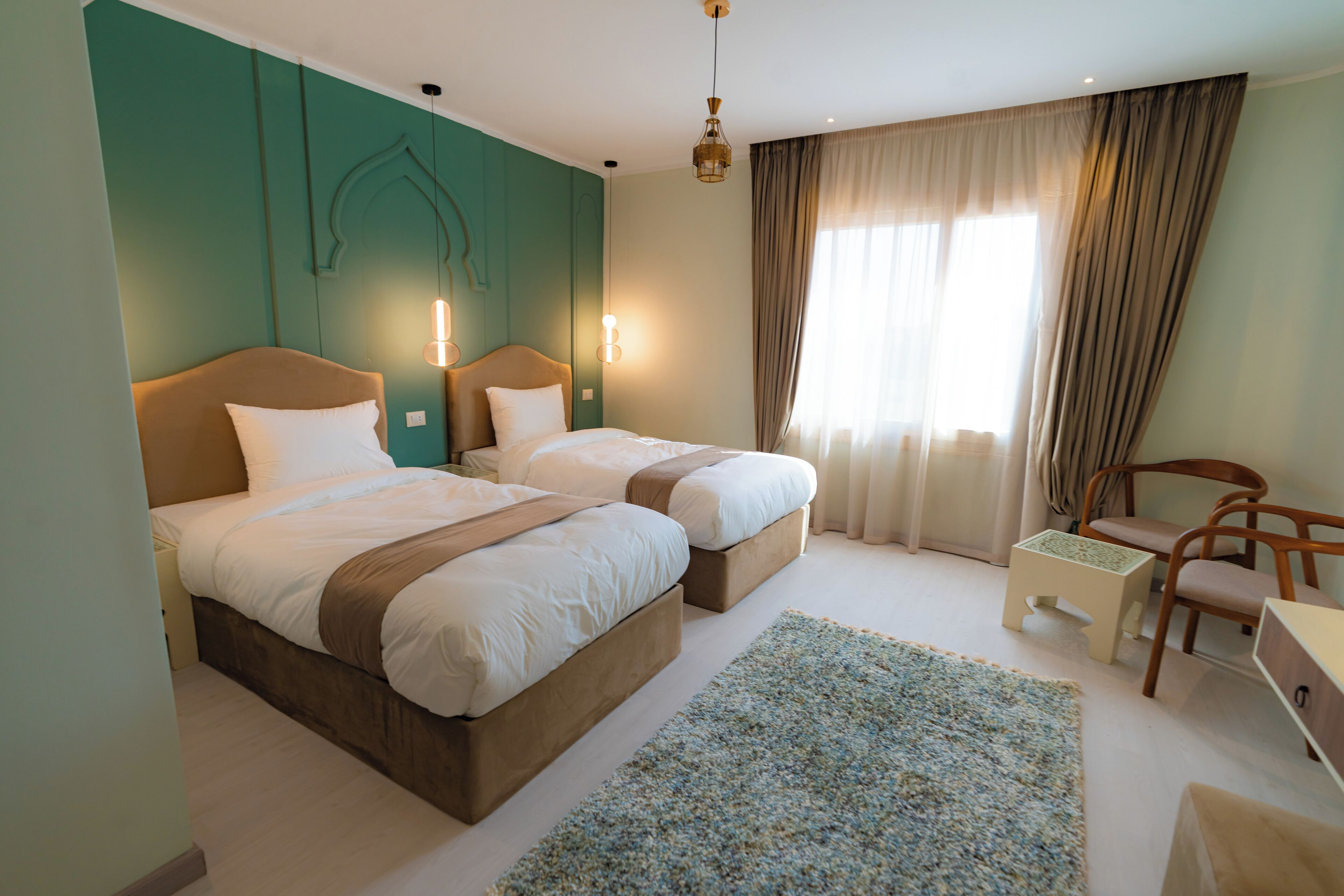A hotel room with two beds, a desk, a chair, and a large window with curtains.