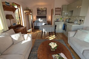 Un salon chaleureux avec un canapé, une table basse agrémentée de fleurs, une table à manger et un coin cuisine équipé de placards et d’appareils électroménagers.