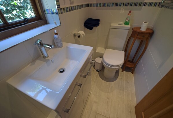 A bathroom with a white sink, toilet, and a wooden side table. - Deer Lodge | A Retreat with Views (Maplehurst)