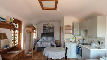 A compact bedroom with a bed, bedside table, and a small desk with a chair. Adjacent is a kitchenette with a stove, sink, and cabinets.