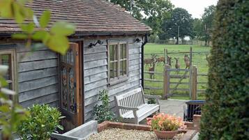 A rustic wooden building with a sloped roof, a bench, and a garden area with flowers and plants.