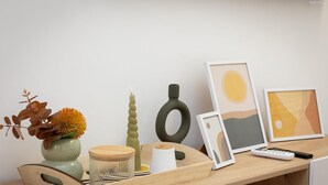 A wooden desk with a vase of dried leaves, a candle, a remote control, and framed artwork. - Rental in Rome Vic House (Rome)