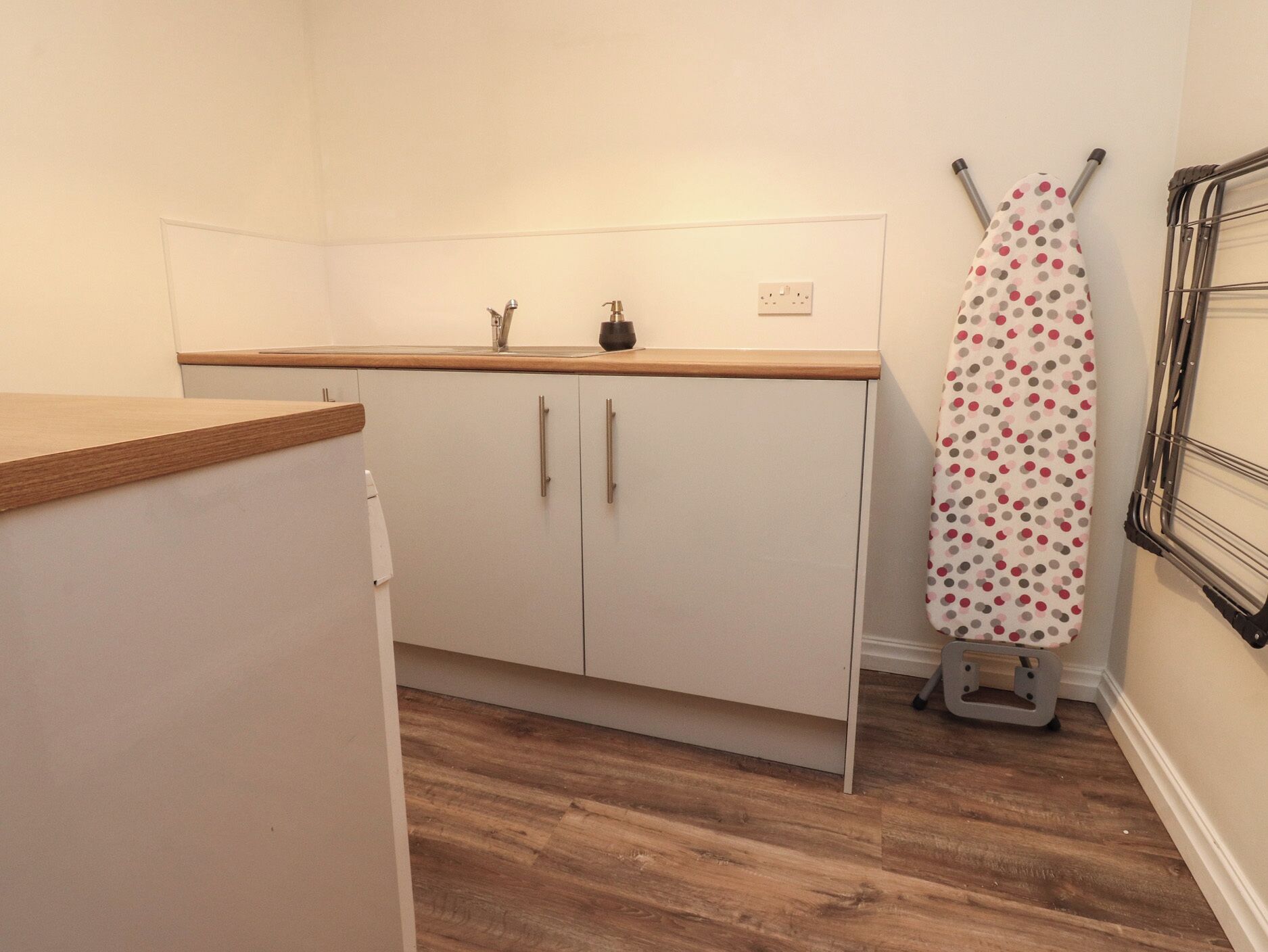 A small kitchen with wooden countertops, white cabinets, and a wall-mounted drying rack.