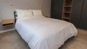 A bedroom with a large bed, a wardrobe, and a small wooden nightstand. - Seaside Serenity (Lytham St. Anne's)