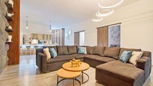 Un salon moderne avec un canapé d’angle, une table basse en bois et une cuisine en arrière-plan.