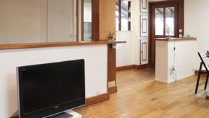 Ein modernes Wohnzimmer mit Flachbildfernseher, Holzboden und einer Küchenzeile mit Schränken und Arbeitsplatte.