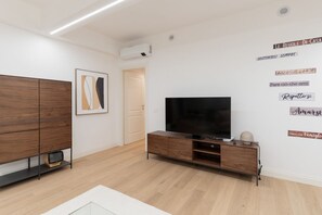 A modern living room with a flat-screen TV, wooden cabinets, and a wall with motivational phrases. - GuestHost - Modern and spacious 96 sqm apartment for 4 guests, located on the semi-basement level of a residential building (stairs to access).The property is just 200 meters from the “De Angeli” M1 Red Line, offering a direct connection to the Duomo (Milan)