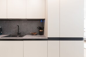 A modern kitchen with a sleek black faucet, a marble backsplash, and minimalist cabinetry. - GuestHost - Modern and spacious 96 sqm apartment for 4 guests, located on the semi-basement level of a residential building (stairs to access).The property is just 200 meters from the “De Angeli” M1 Red Line, offering a direct connection to the Duomo (Milan)
