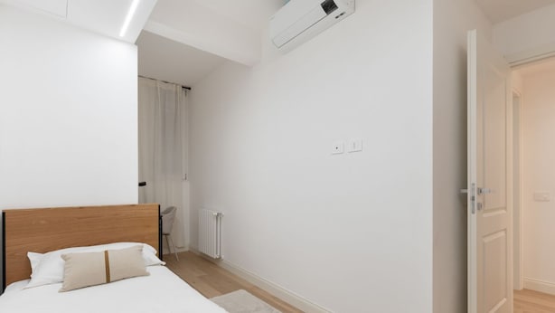 Ein Schlafzimmer mit einem Holzkopfteil, einem Bett mit weißen Leinentüchern, einem Heizkörper und einer weißen Tür.