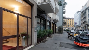 Ein Hotelzugang mit Glastüren, einem roten Teppich, Blumentöpfen und einem abgestellten Motorrad.