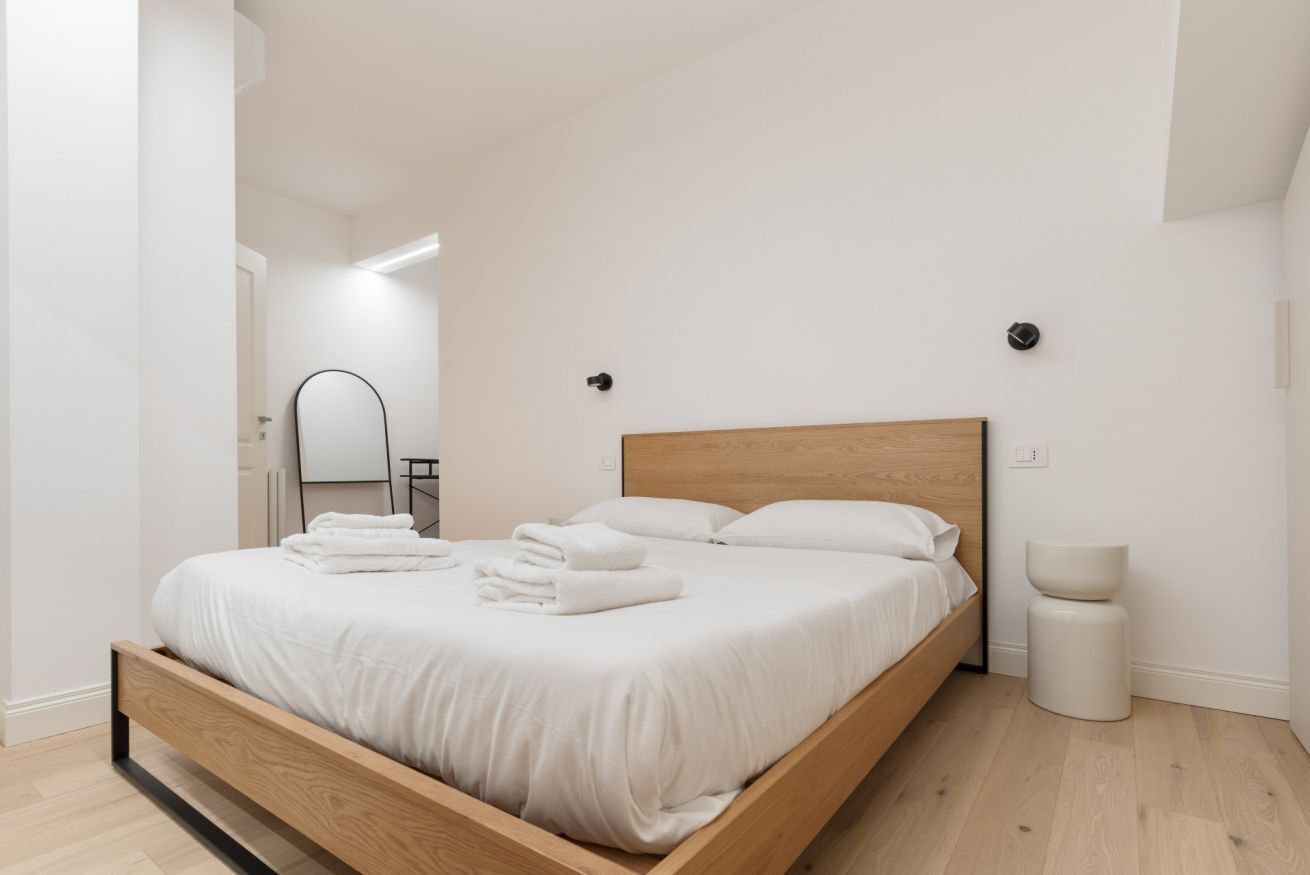 A modern bedroom with a wooden bed, white linens, and a small bedside table.