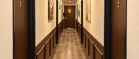 A hotel corridor with wooden flooring, double doors, and framed artwork on the walls.
