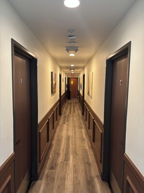 A hotel hallway with wooden floors, doors on both sides, and overhead lighting.