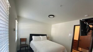 A hotel room with a single bed, a chair, a desk, and a door leading to another room. - Country Lodge (Big Bear Lake)
