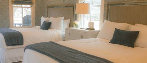 A hotel room with two beds, a nightstand, a lamp, and a window with curtains.