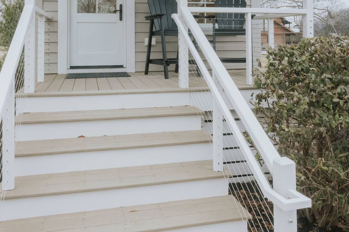 A house with a white exterior, a front door, a porch with a railing, a chair, and a small table.