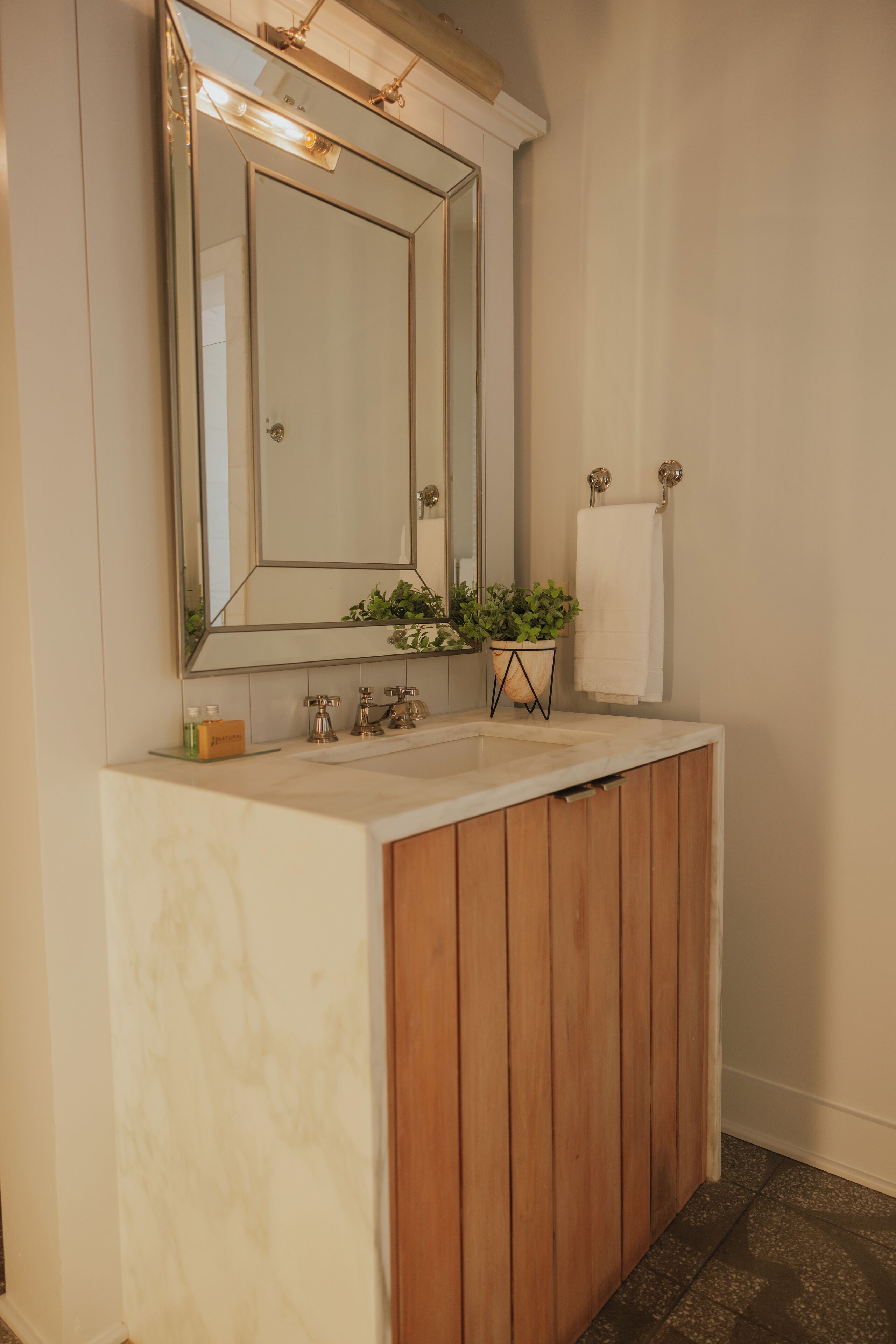 A bathroom with a wooden vanity, a large mirror, a sink, and a potted plant.