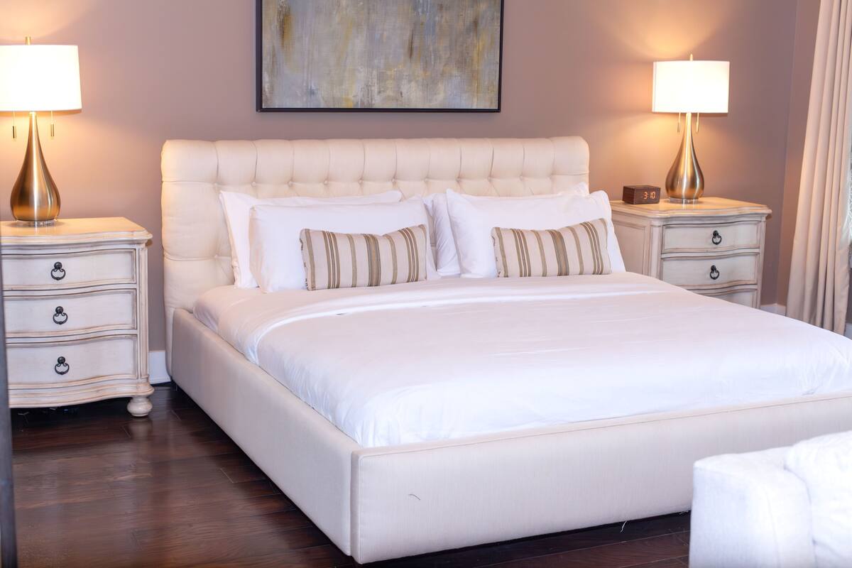 A large bed with a tufted headboard, two bedside tables with lamps, and a clock on one of the tables.