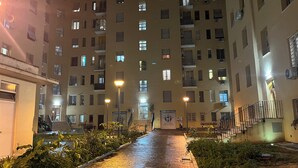 Vista nocturna de un edificio residencial de varios pisos, suelo mojado, farolas y un letrero de un estudio dental.
