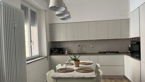 Una cocina moderna con armarios blancos, encimera de mármol y comedor con mesa y sillas blancas.