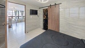 Ein modernes Schlafzimmer mit Bett, einem an der Wand befestigten Fernseher und einer Schiebetür, die auf einen Balkon führt.