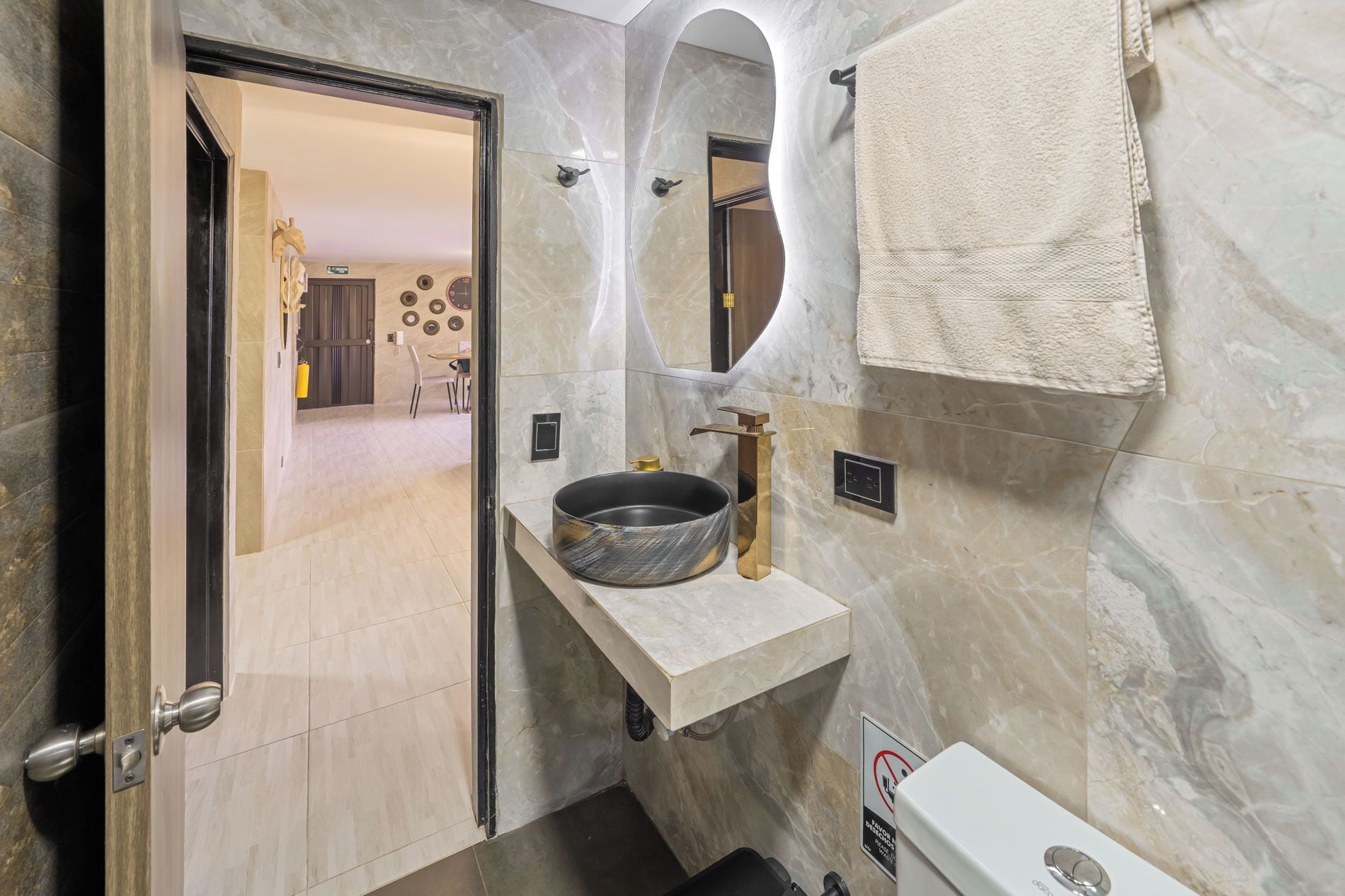 Ein modernes Badezimmer mit einem мраморному Waschbecken, einem runden Spiegel und einem Handtuch an der Wand.