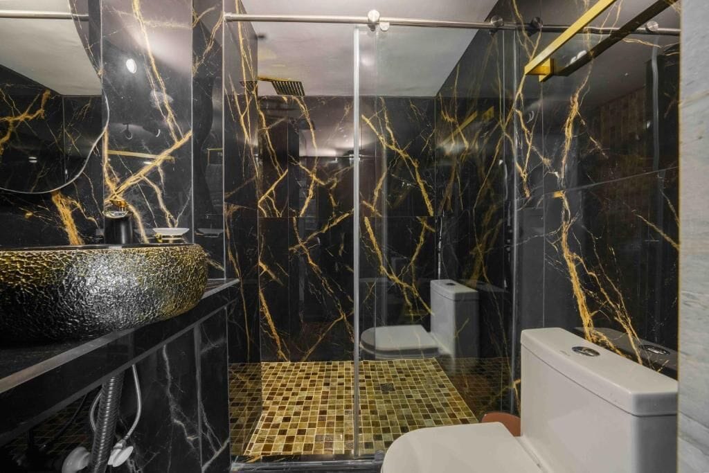 Un bagno moderno con una parete in marmo nero, un box doccia in vetro e un water bianco.