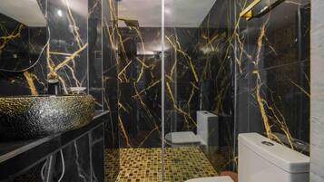 Un bagno moderno con una parete in marmo nero, un box doccia in vetro e un water bianco.