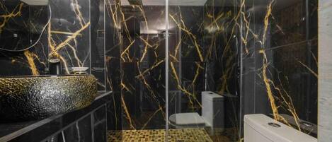 Un baño moderno con pared de mármol negro, cabina de ducha de vidrio y un inodoro blanco.