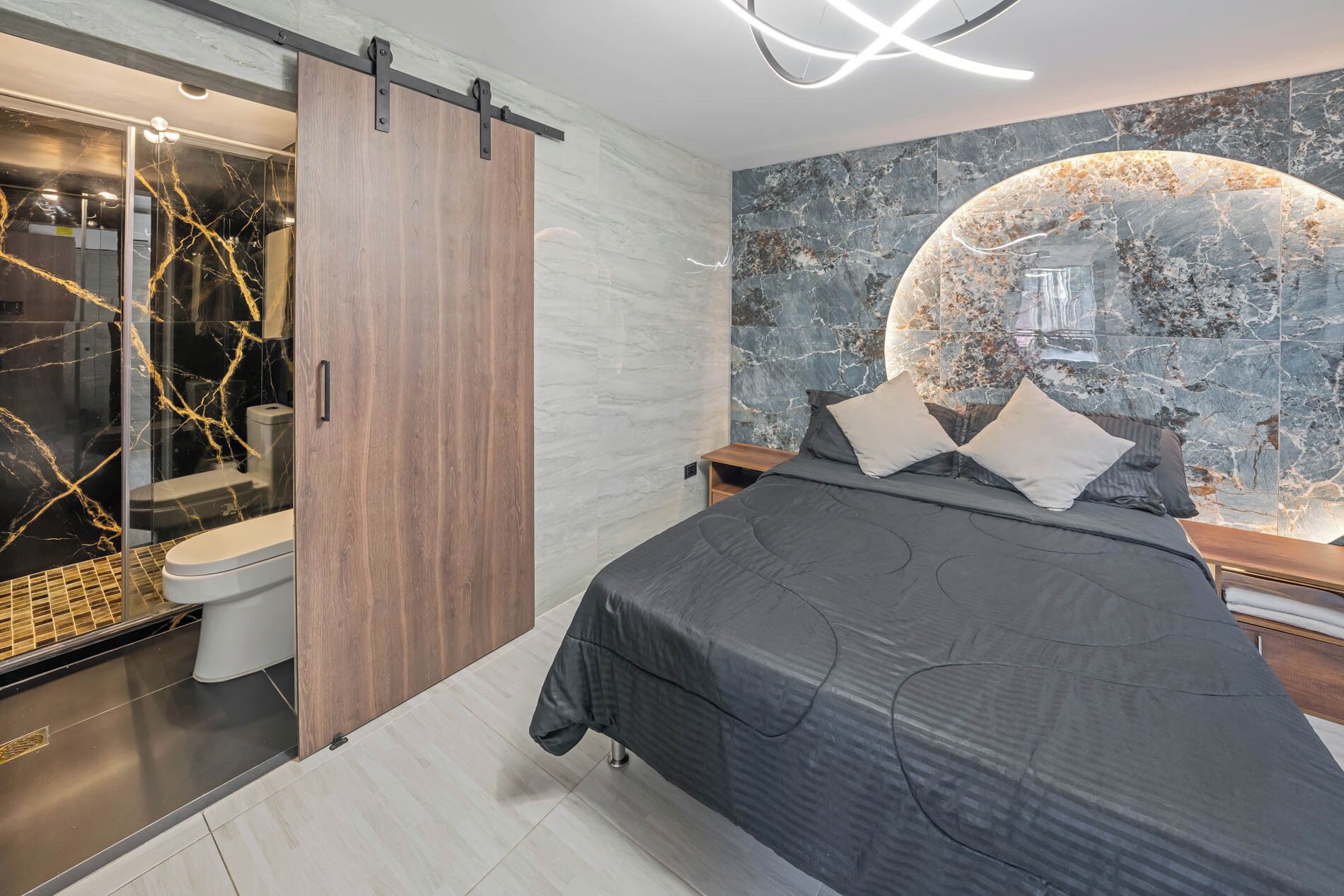 A modern bedroom with a bed, a bathroom with a glass shower, and a marble wall.