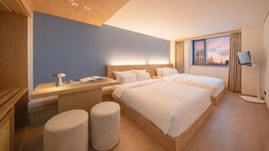 Habitación de hotel moderna con techo de madera, dos camas, un escritorio con lámpara, un televisor y una ventana con vista al atardecer.