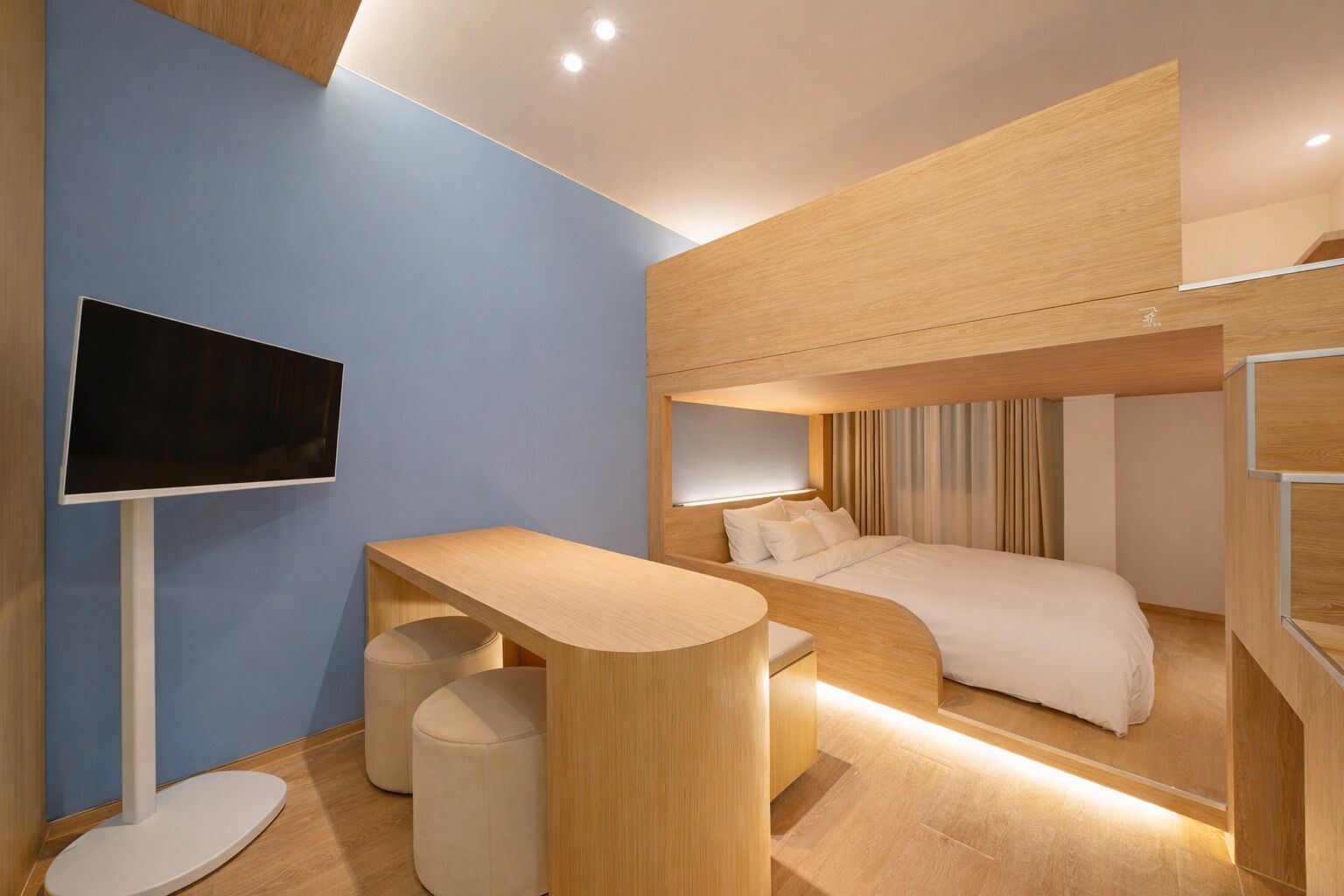 Une chambre d’hôtel moderne équipée d’un lit superposé, d’un bureau, d’une télévision et d’un petit coin salon.