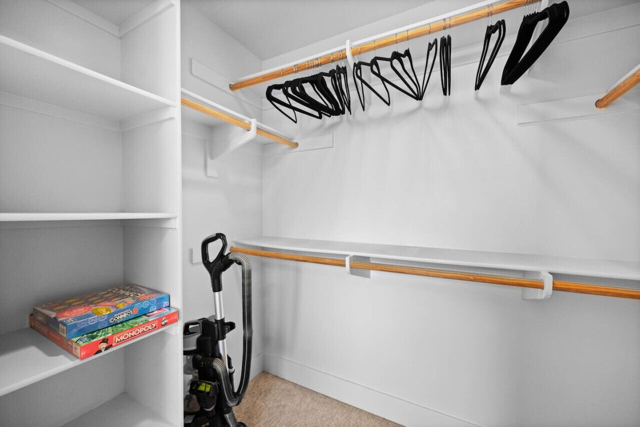 A closet with shelves, a vacuum cleaner, and a rack with black items.
