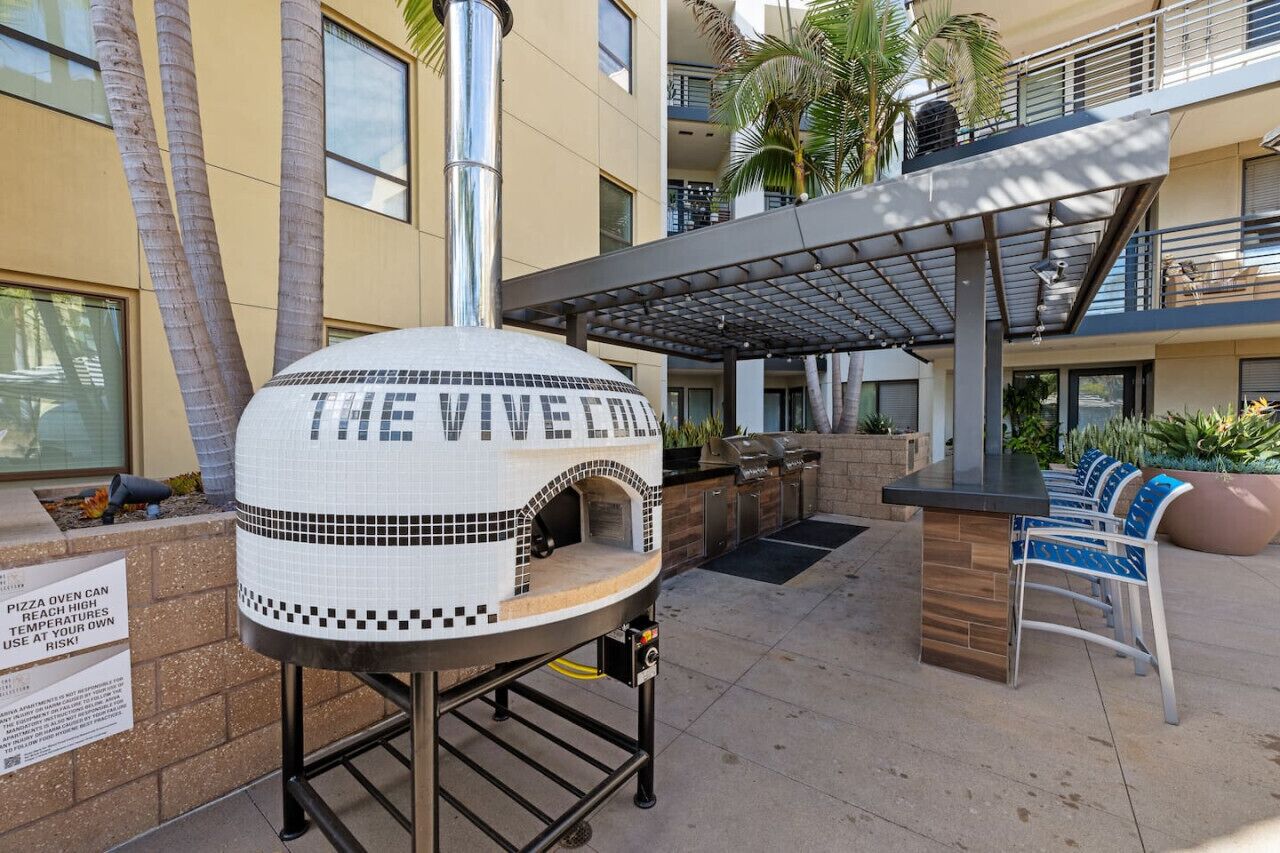 Forno per pizza all'aperto con l'insegna "The Vibe Oven" e un cartello che avverte dei rischi dovuti all'alta temperatura.