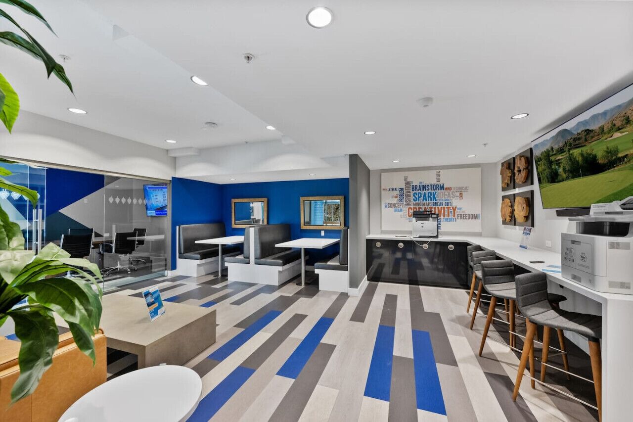 A modern office space with a blue and white color scheme, featuring a reception area, seating arrangements, and a large screen displaying information.