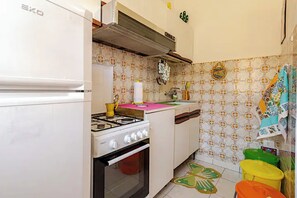 A compact kitchen with a white refrigerator, a stove, and a sink. The walls are decorated with patterned tiles. - AT THE VERANDA BEAM (Vittoria)